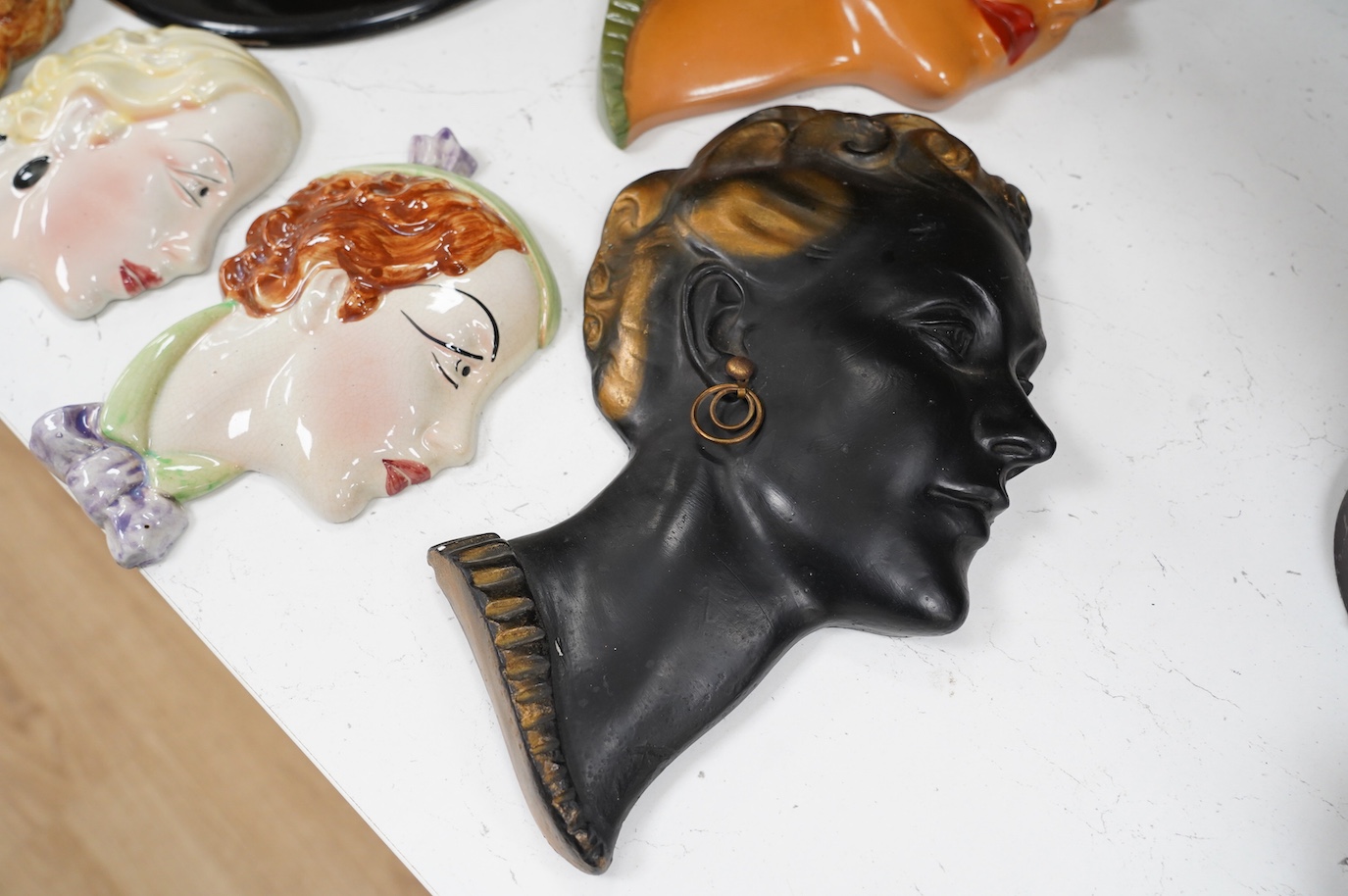 Six Art Deco style composition and pottery wall masks, largest 30cm high. Condition - fair, one mask detached from plaque